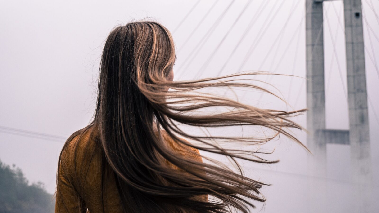 Kobieta ze zdrowymi włosami stojąca przed mostem